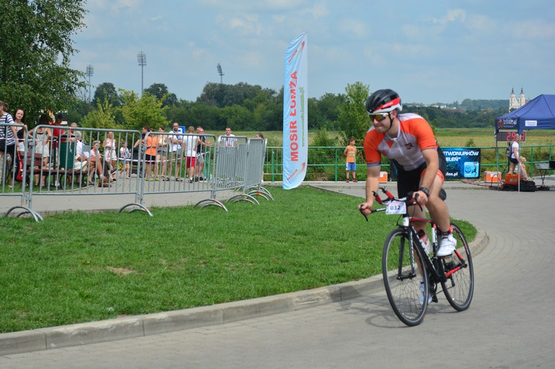 zdjęcie przedstawiające zawodnika triathlonu jadącego na rowerze na terenie łomzyńskich bulwarów, w tle kibice