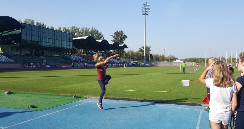 dziewczyna rzucająca piłeczką palantową, w tle murawa i budynek stadionu