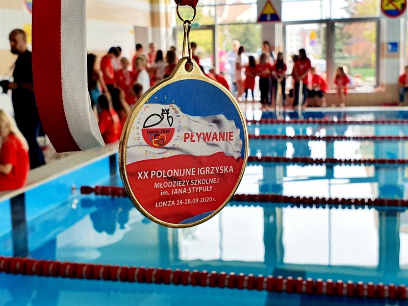zdjęcie medal, w tle basen i zawodnicy zawodów pływackich