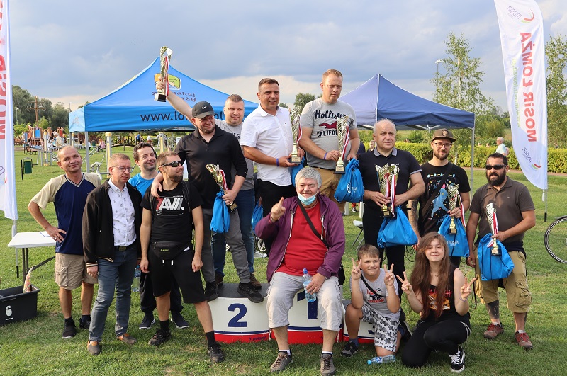 grupa zawodników na podium z pucharami w dłoniach, w tle łomżyńskie bulwar