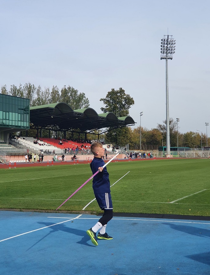 zdjęcie mężczyzny rzucającego oszczepem na stadionie, w tle murawa,  budynek stadionu miejskiego w Łomży