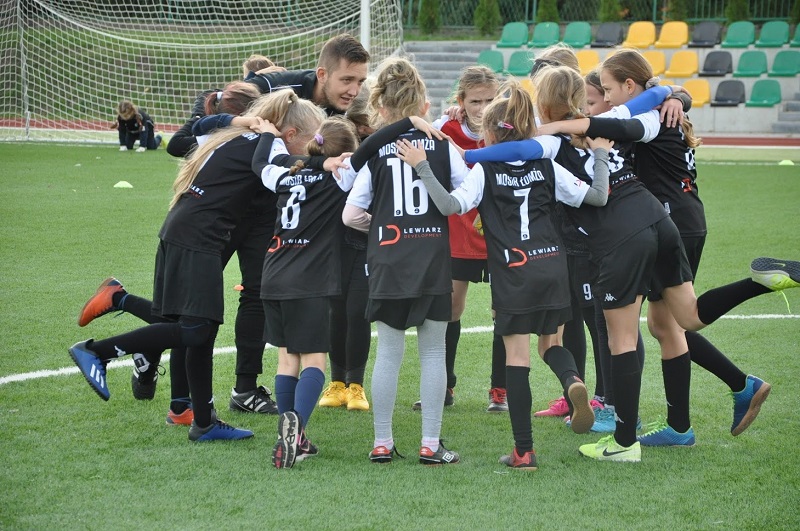 Na zdjęciu stoi grupa zawodniczek trzymająca się za ramiona i szykująca się do okrzyku.