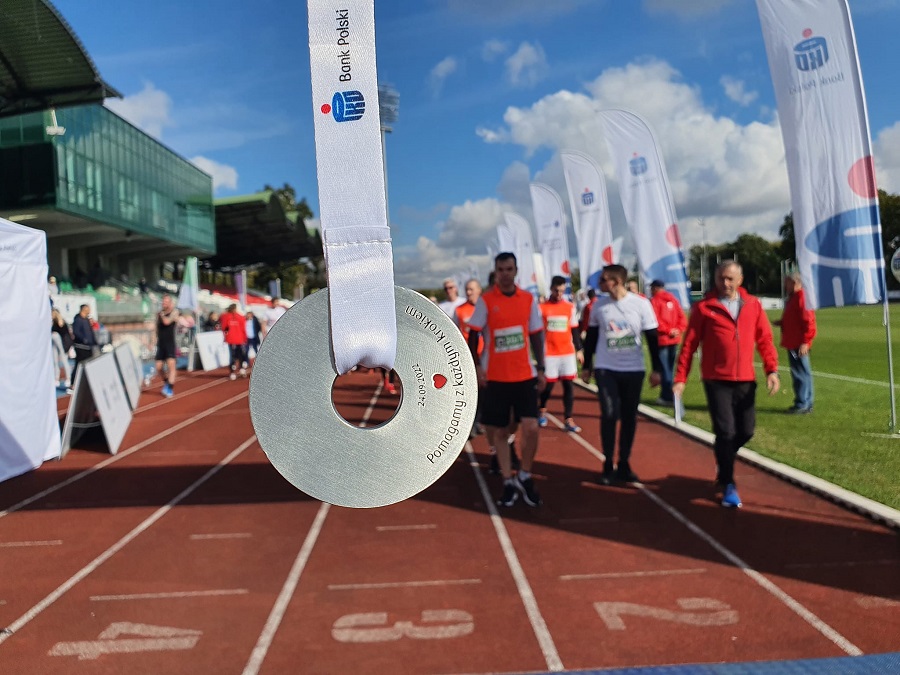 zdjęcie przedstyawiające medal 6. biegu pko charytatywnego, w tle grupa osób biegnie po bieżni stadionu