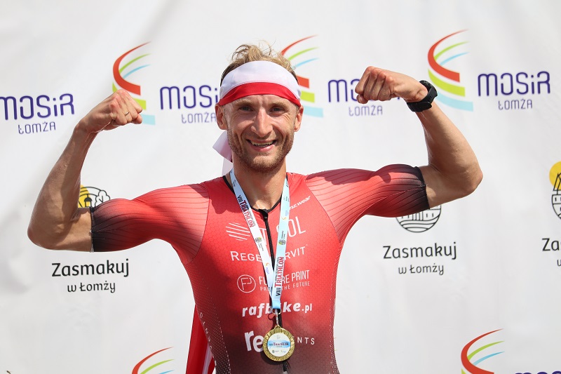 zdjęcie przedstawiające zwycięzcę triathlonu na tle ścianki z logo mosir