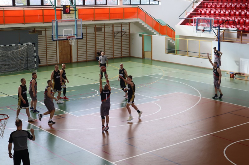 Zdjęcie przedstawia zawodników dwóch drużyn grających w koszykówkę na Hali Sportowej.