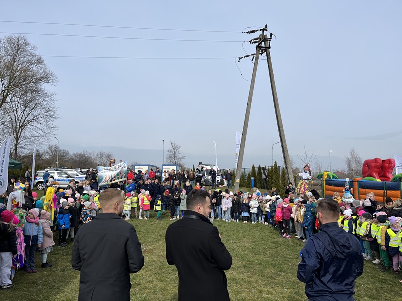 3 osoby na pierwszym planie stojące tyłem, a w tle dużo dzieci