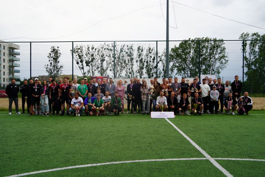 Grupa zawodników Miejskiej Ligi Piłki Nożnej MOSiR Łomża z trofeami na tle murawy boiska Orlik
