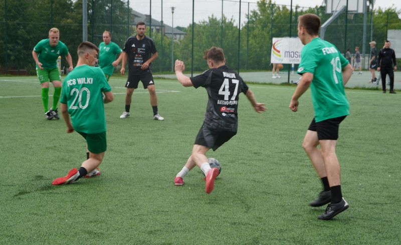 Zawodnicy Miejskiej Ligi Piłki Nożnej grający w piłkę na murawie boiska Orlik