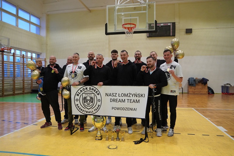Zdjęcie przedstawia zwycięską drużynę MLK MOSiR Łomża. Na zdjęciu zawodnicy trzymają baner oraz trofea sportowe.