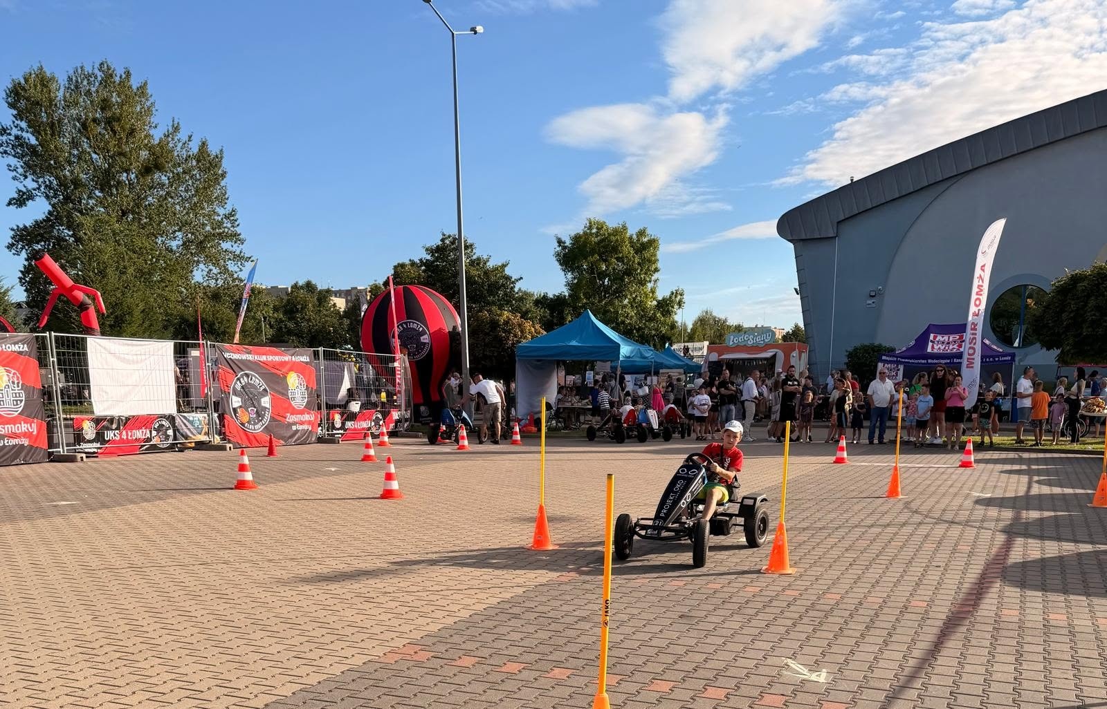 Zdjęcie przedstawia dziecko jeżdżące na gokarcie na parkingu